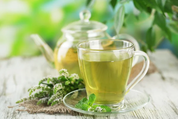 Чайник и чашка травяного чая со свежими мятными цветами на деревянном столе — стоковое фото