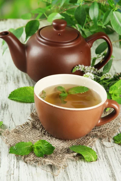 Konvice a šálek bylinného čaje s čerstvou mátou květy na dřevěný stůl — Stock fotografie