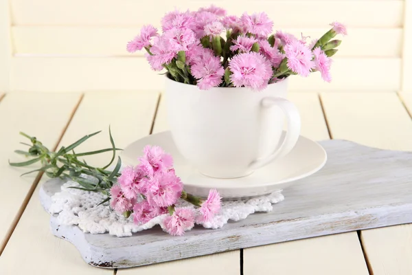 Muchos pequeños dientes de color rosa en taza sobre tabla de madera sobre fondo beige —  Fotos de Stock