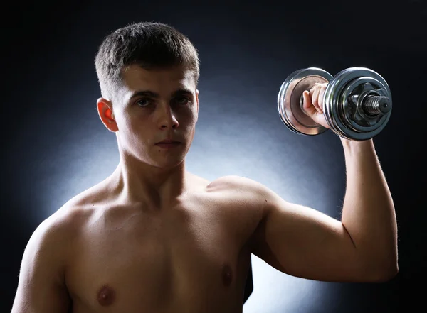 Bonito jovem desportista muscular executar exercício com halteres no fundo escuro — Fotografia de Stock