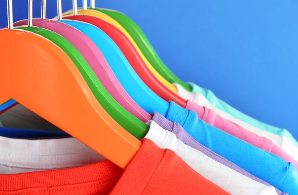 Different shirts on colorful hangers on blue background — Stock Photo, Image