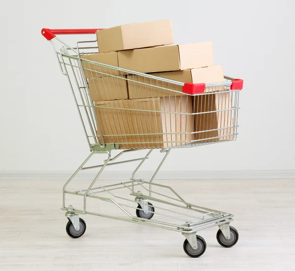 Shopping cart with carton, on gray background — Stock Photo, Image