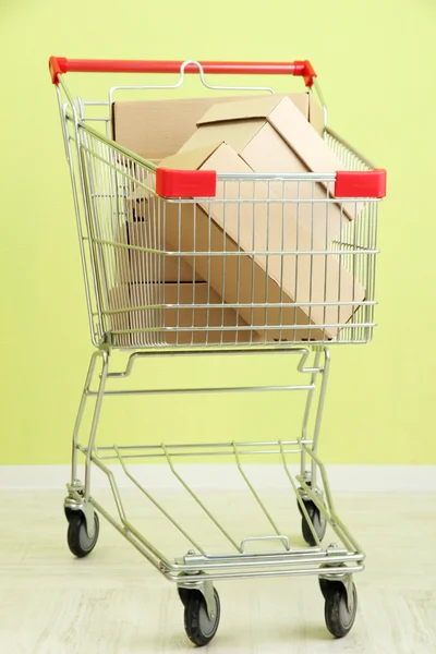 Shopping cart with carton, on green wall background — Stock Photo, Image