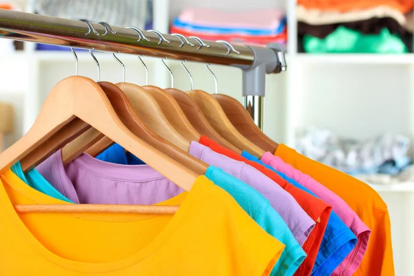 Variedad de camisetas casuales en perchas de madera en los estantes de fondo —  Fotos de Stock