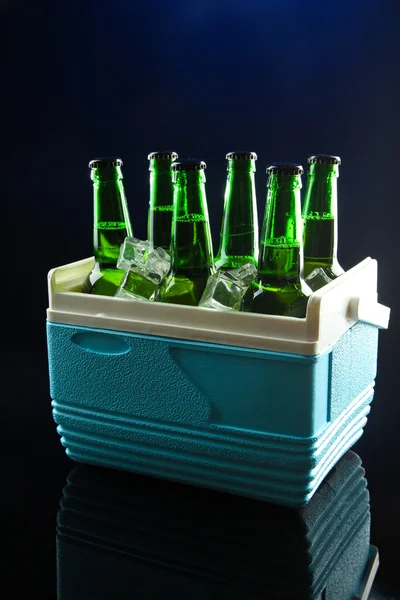 Botellas de cerveza con cubitos de hielo en mini nevera, sobre fondo azul oscuro — Foto de Stock