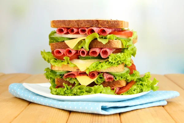 Huge sandwich on wooden table, on light background — Stock Photo, Image