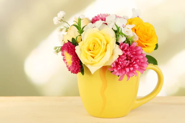 Schöner Strauß heller Blumen in farbigem Becher, auf Holztisch, auf hellem Hintergrund — Stockfoto