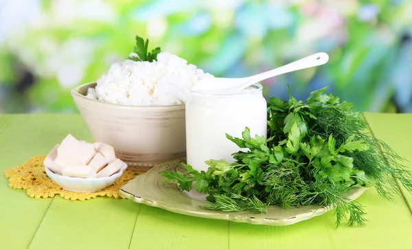 Čerstvé mléčné výrobky s zelení na dřevěný stůl na přírodní pozadí — Stock fotografie