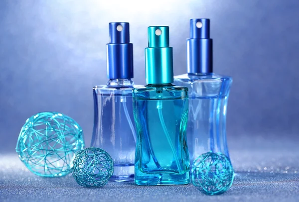 Perfume de mujer en hermosas botellas sobre fondo azul — Foto de Stock