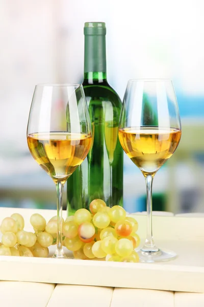 Ripe grapes, bottle and glasses of wine on tray, on bright background