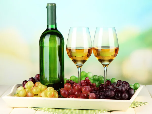 Érett szőlő, a palack és a pohár bor a tálca, a világos háttér — Stock Fotó