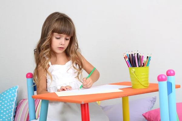 Menina desenha sentado à mesa no quarto no fundo da parede cinza — Fotografia de Stock