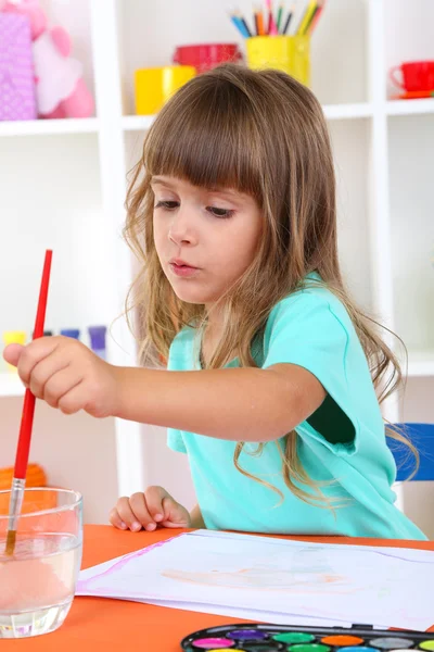 Petite fille dessine assis à table dans la chambre sur des étagères fond — Photo