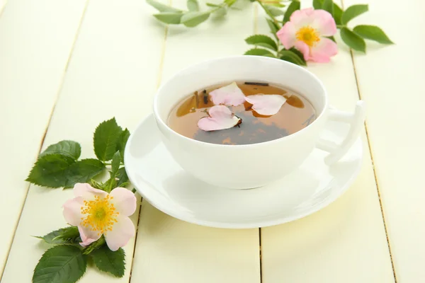 Xícara de chá de ervas com flores de rosa do quadril na mesa de madeira branca — Fotografia de Stock