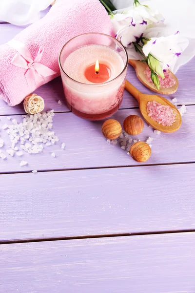 Beautiful spa setting with pink candle and flowers on purple wooden background — Stock Photo, Image