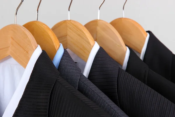 Suits with shirts on hangers on light background — Stock Photo, Image