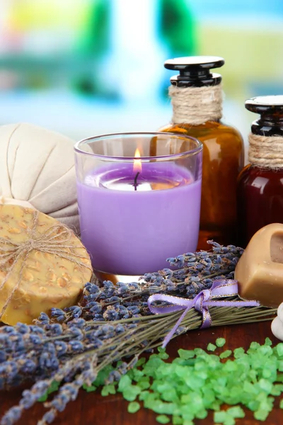 Natura morta con candela alla lavanda, sapone, palle da massaggio, bottiglie, sapone e lavanda fresca, su tavolo di legno su sfondo luminoso — Foto Stock