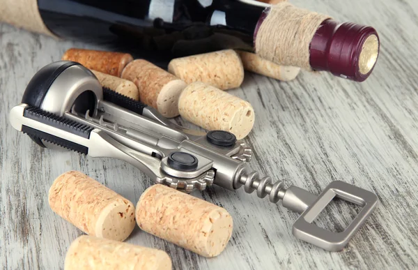 Corkscrew with wine corks and bottle of wine on wooden table close-up — Stock Photo, Image
