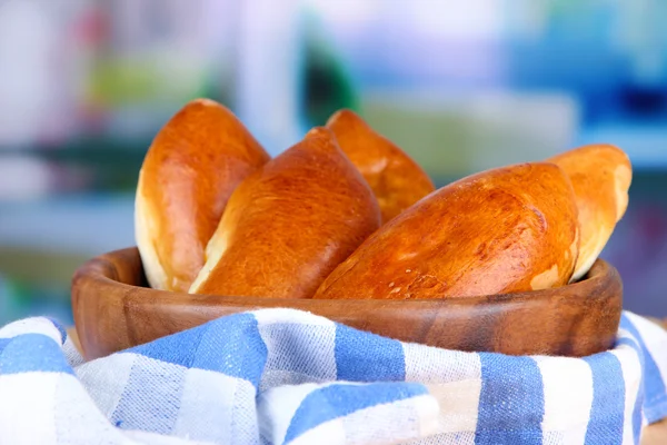 Fresh baked pasties, in wooden bowl, on wooden table, on bright background — Stock Photo, Image