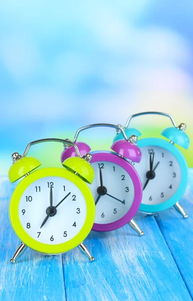 Relojes de alarma de colores en la mesa sobre fondo azul — Foto de Stock