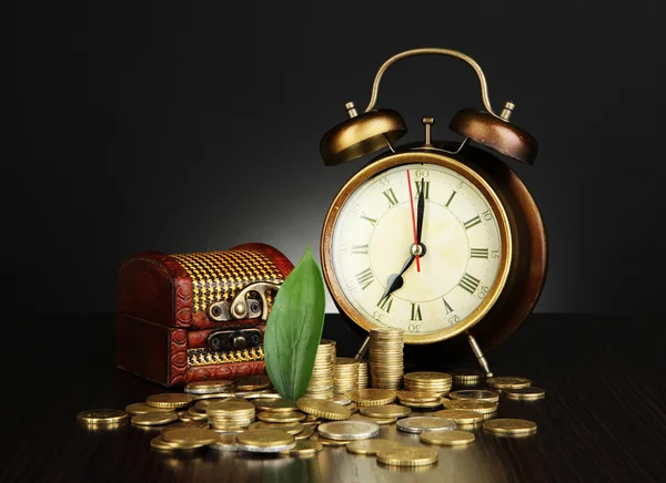 Antieke clock en munten op houten tafel op donkere kleur achtergrond — Stockfoto