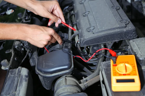Bilmekaniker använder multimetern voltmeter för att kontrollera spänningsnivån i batteriets — Stockfoto