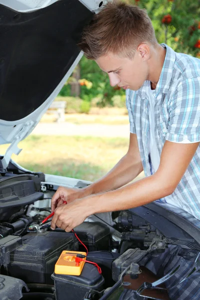 Conductor joven utiliza voltímetro multímetro para comprobar el nivel de voltaje en la batería del coche —  Fotos de Stock