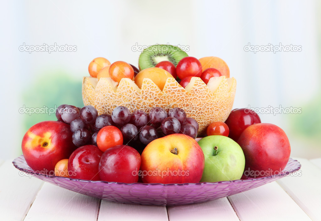 Assortment of juicy fruits on wooden table, on bright background