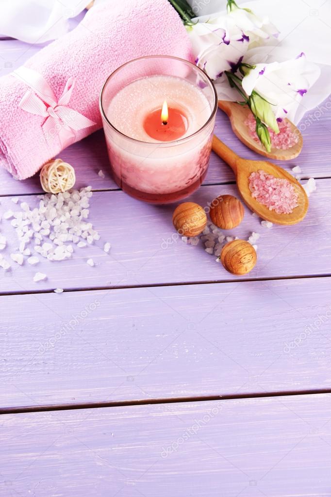Beautiful spa setting with pink candle and flowers on purple wooden background