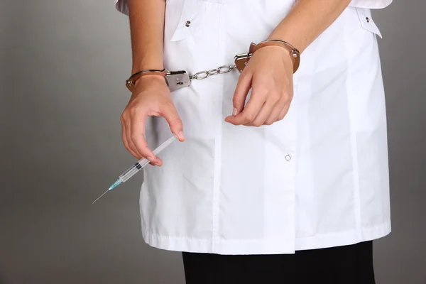 Doctor with syringe in handcuffs on grey background — Stock Photo, Image