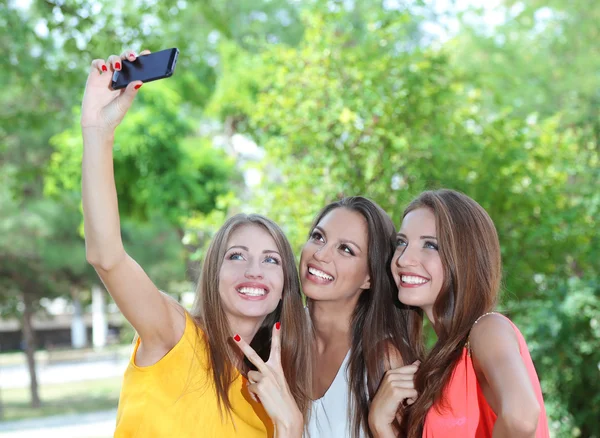 Tres hermosas mujeres jóvenes tomando fotos en el parque de verano —  Fotos de Stock