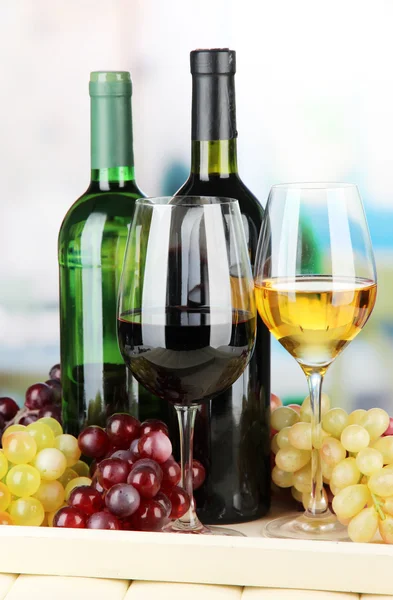 Wine bottles and glasses of wine on tray, on bright background — Stock Photo, Image