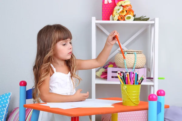 Klein meisje trekt vergadering aan tafel in kamer op grijs muur achtergrond — Stockfoto