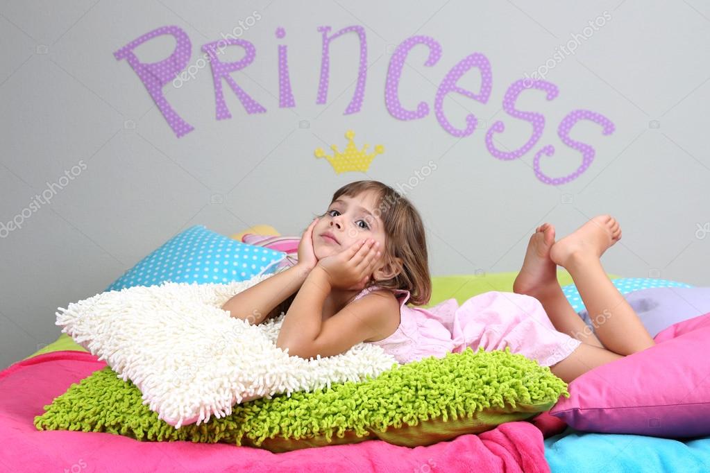 Little girl lying on bed in room on grey wall background Stock Photo by