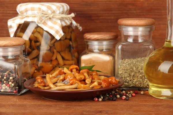 Composition of delicious marinated mushrooms, oil and spices on wooden table on wooden background