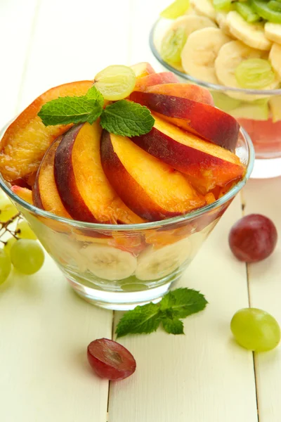 Salade de fruits savoureuse dans des bols en verre, sur une table en bois blanc — Photo