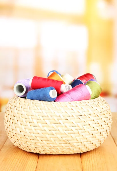 Wicker basket with accessories for needlework on wooden table, on bright background — Stock Photo, Image