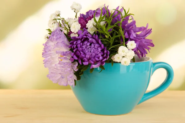 Hermoso ramo de flores brillantes en taza de color, sobre mesa de madera, sobre fondo brillante — Foto de Stock