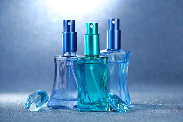 Perfume de mujer en hermosas botellas sobre fondo azul — Foto de Stock