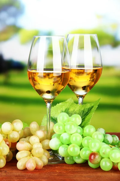Ripe grapes and glasses of wine, on bright background — Stock Photo, Image