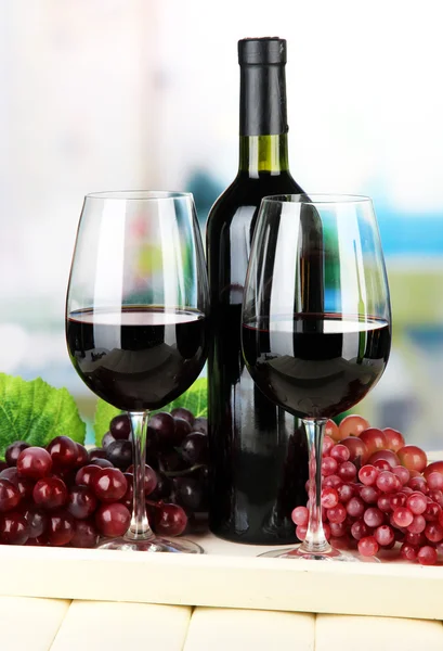 Uve mature, bottiglia e bicchieri di vino su vassoio, su sfondo brillante — Foto Stock