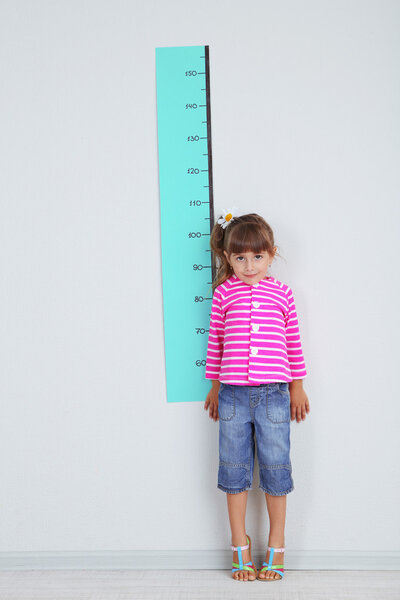 Little girl measuring height against wall in room