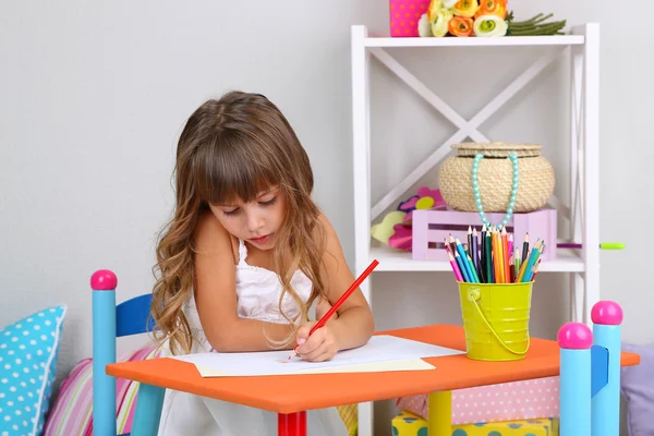 Bambina disegna seduto a tavola in camera su sfondo grigio parete — Foto Stock