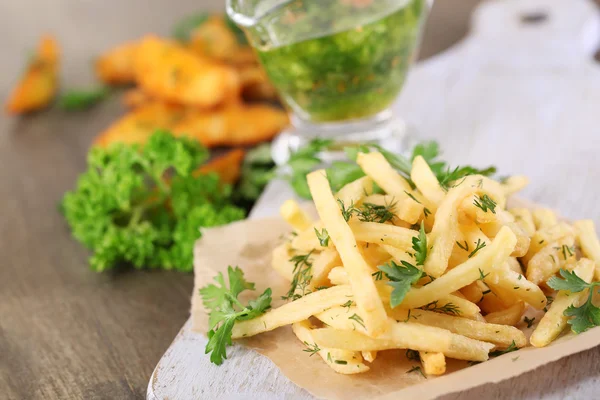 French fries on tracing paper on board on wooden table — Stock Photo, Image