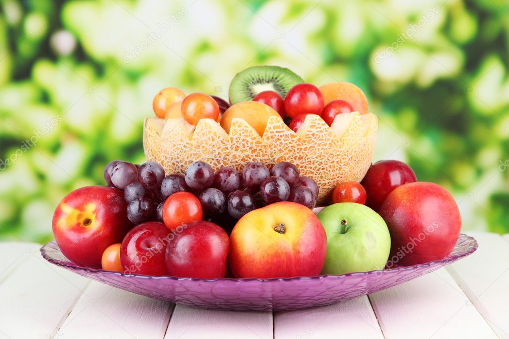 Assortment of juicy fruits on wooden table, on bright background