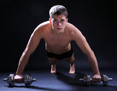 yakışıklı genç kaslı sporcu, koyu arka plan üzerinde egzersiz halter ile yürütmek