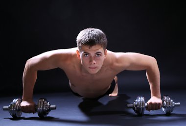 yakışıklı genç kaslı sporcu, koyu arka plan üzerinde egzersiz halter ile yürütmek