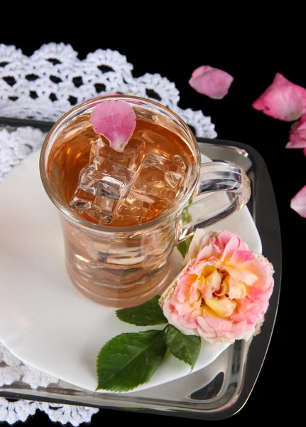 Glass cup of ice tea from tea rose on metallic tray on napkin on black background