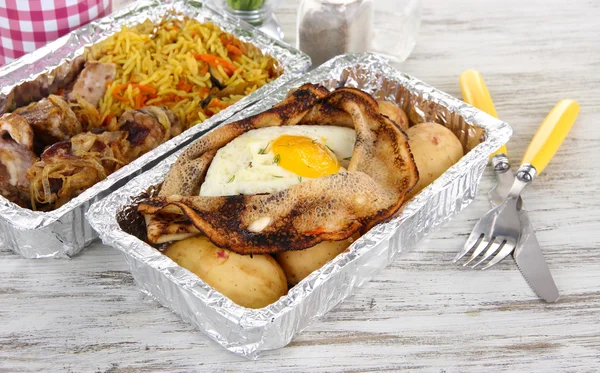 Food in boxes of foil on wooden table — Stock Photo, Image