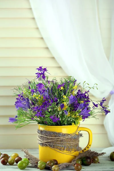 Beautiful bouquet of wildflowers in cup and berries on wooden table — Stock Photo, Image